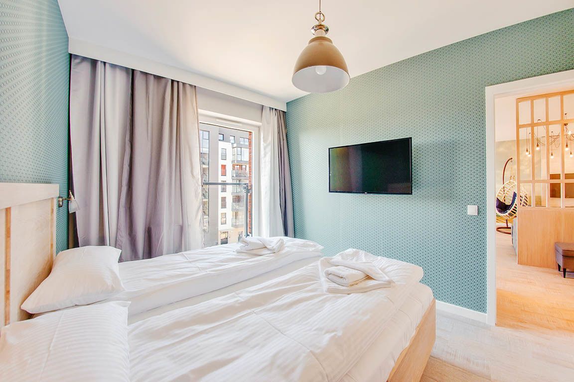 A hotel room with two beds, a TV on the wall, and a view of the city through the window.