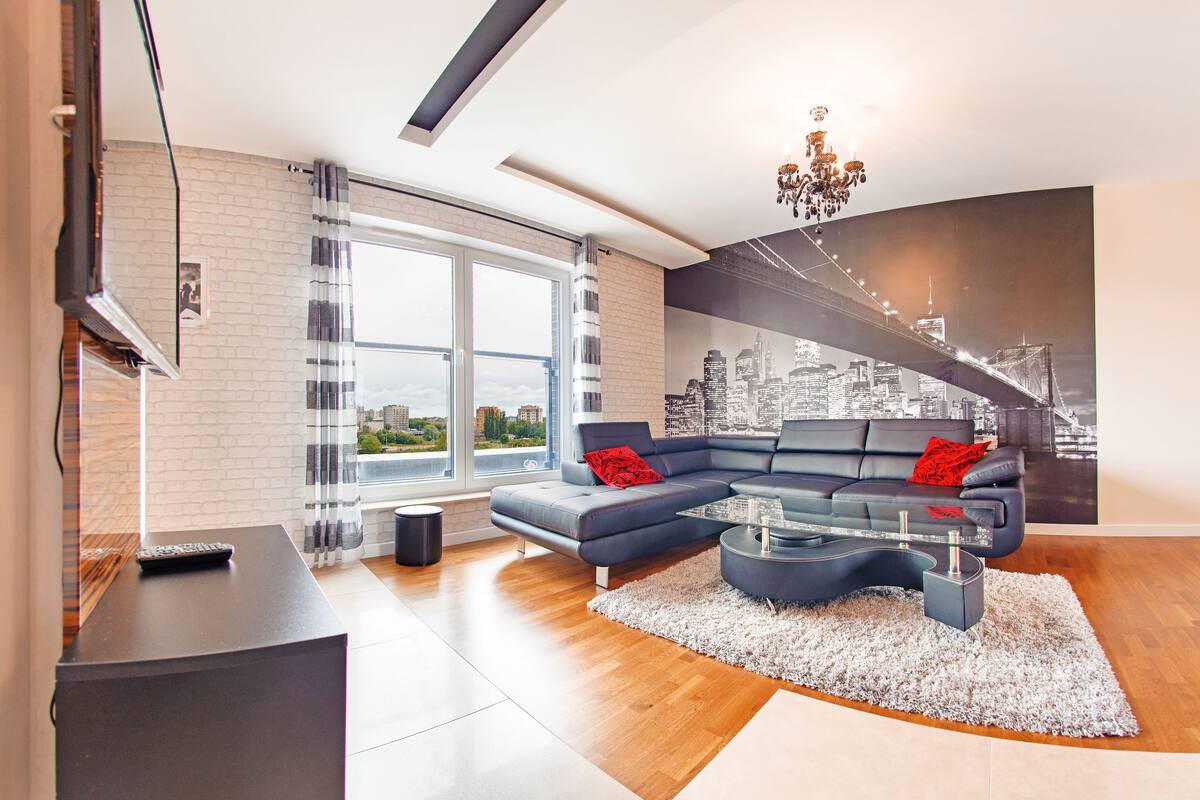 Un salon moderne avec un canapé d’angle, une table basse en verre et une fresque représentant un paysage urbain sur le mur.