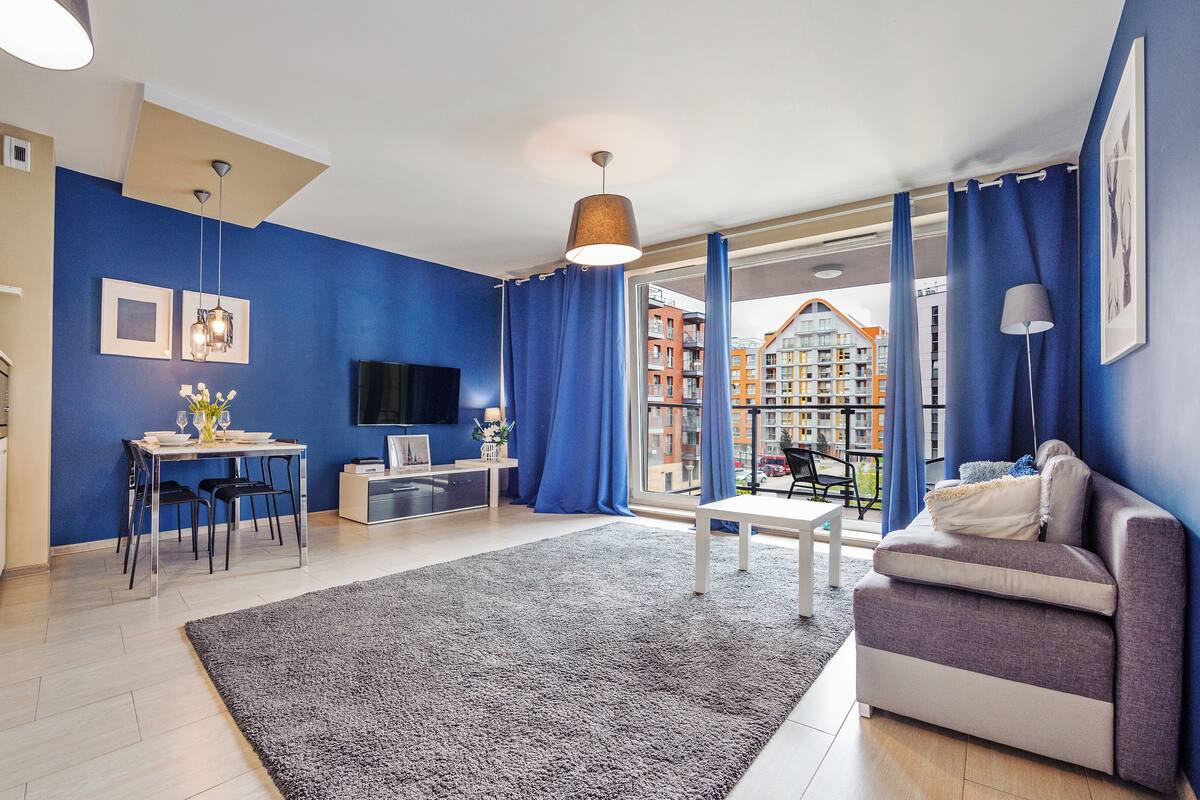Un salon moderne comprenant un coin repas, un canapé, un téléviseur et un balcon offrant une vue sur les immeubles.