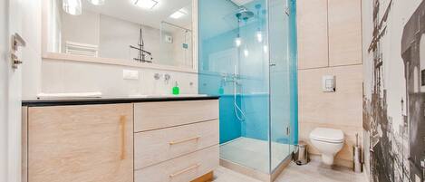 A modern bathroom with a glass shower enclosure, a toilet, and a vanity with drawers.