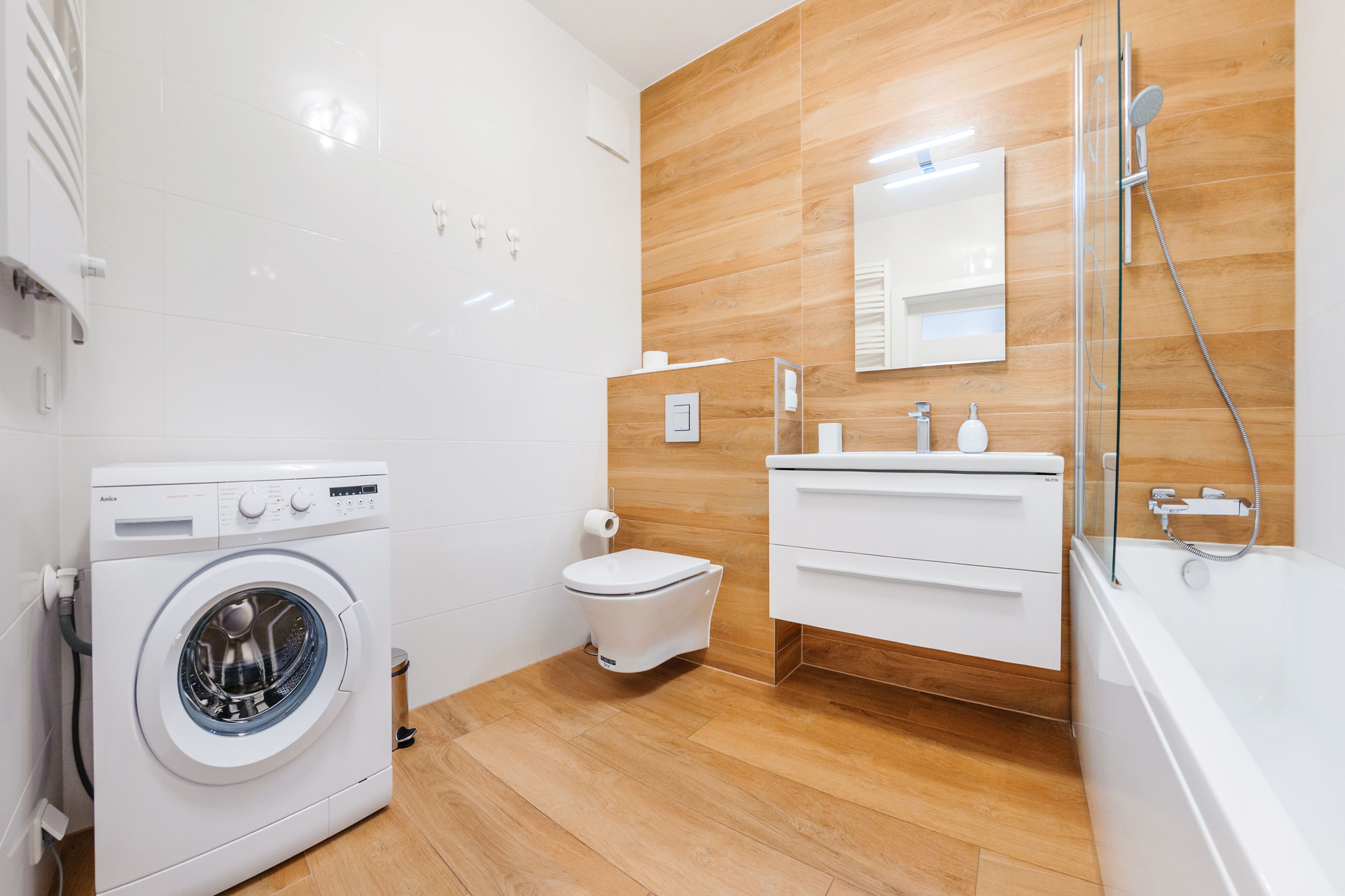 A modern bathroom with a washing machine, toilet, vanity, and bathtub.