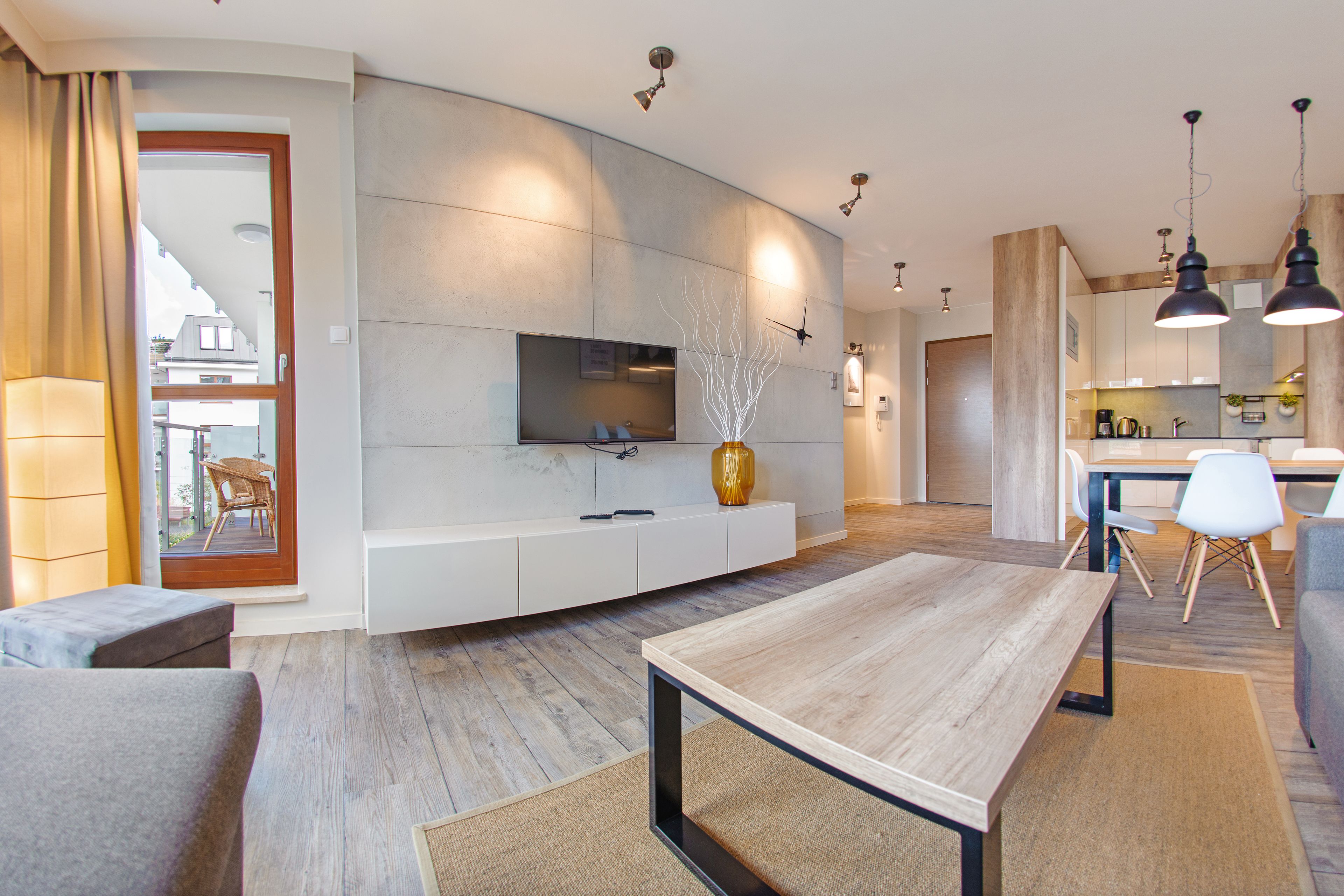 A modern living room with a wooden dining table, a sofa, and a TV mounted on a white cabinet.