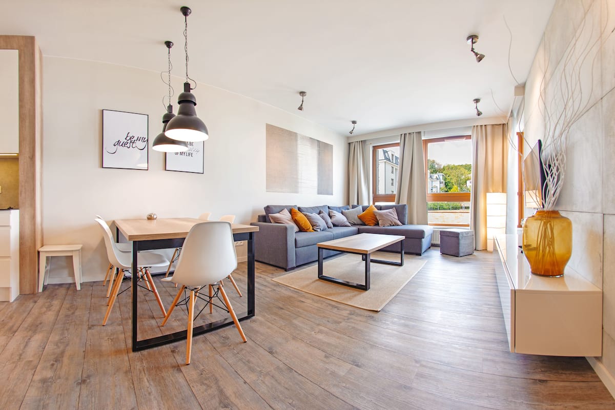 Ein modernes Wohnzimmer mit Sofa, Couchtisch und Esstisch. An den Wänden hängen Bilder und auf der Anrichte steht eine Vase.