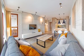 Un soggiorno moderno con divano, tavolino e TV. In secondo piano, un'area cucina.