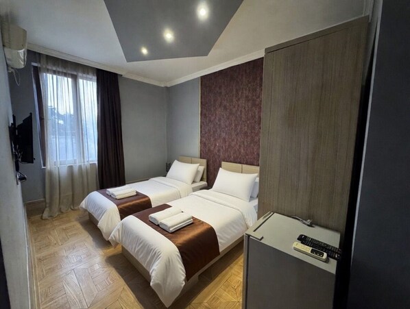 A hotel room with two beds, a desk, a TV, and a window with curtains. - HOTEL ELİTE (Batumi)
