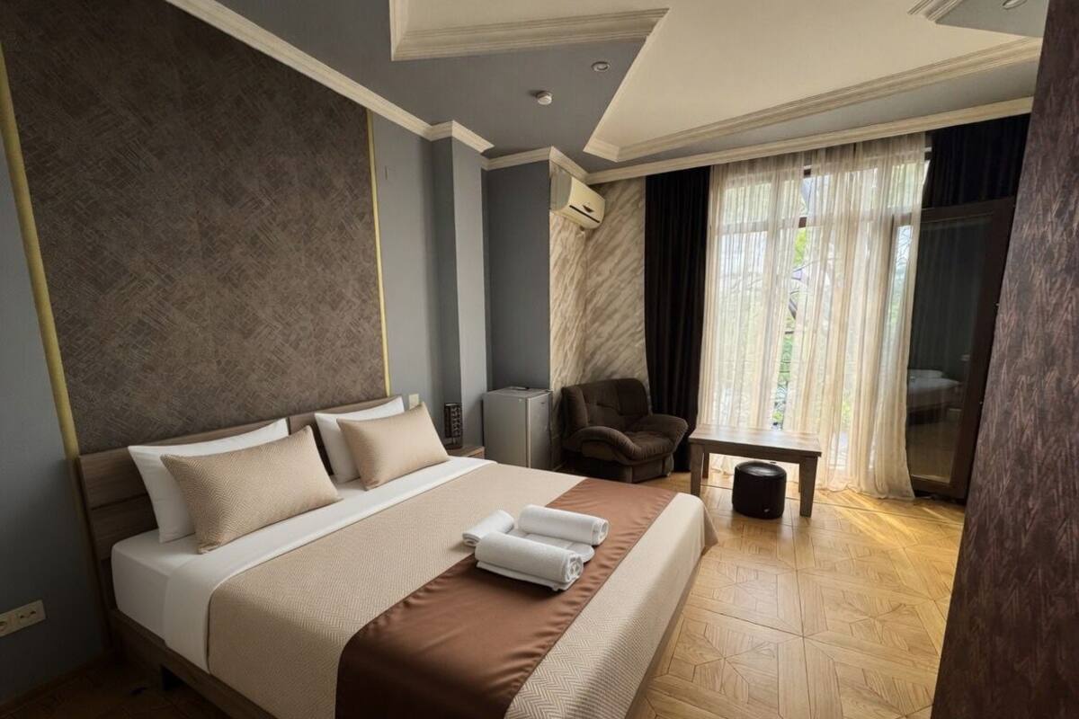 Ein Hotelzimmer mit einem großen Bett, einem Sessel, einem kleinen Tisch und Blick ins Freie.