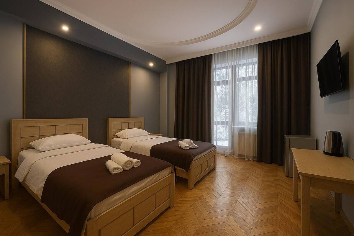 Ein Hotelzimmer mit zwei Betten, einem Schreibtisch, einem Fernseher und einem Fenster mit Vorhängen.
