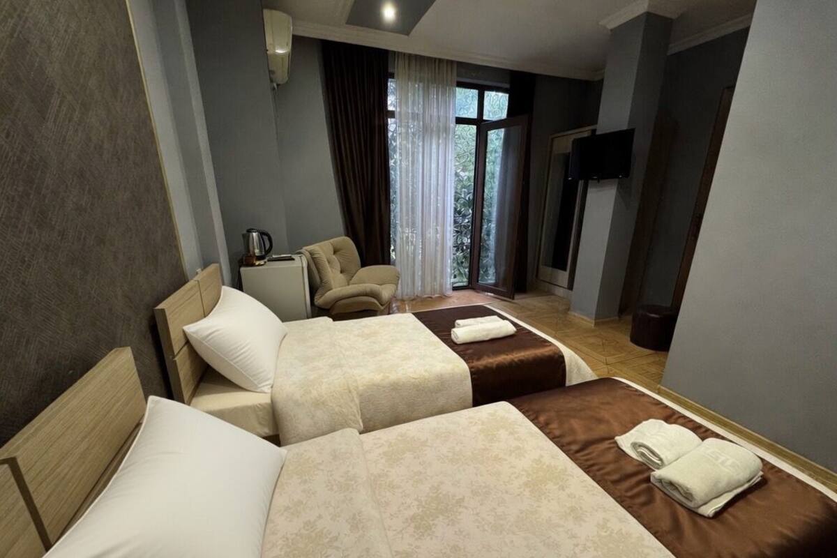 Ein Hotelzimmer mit zwei Betten, einem Sessel, einem Fernseher und einem Fenster mit Vorhängen.