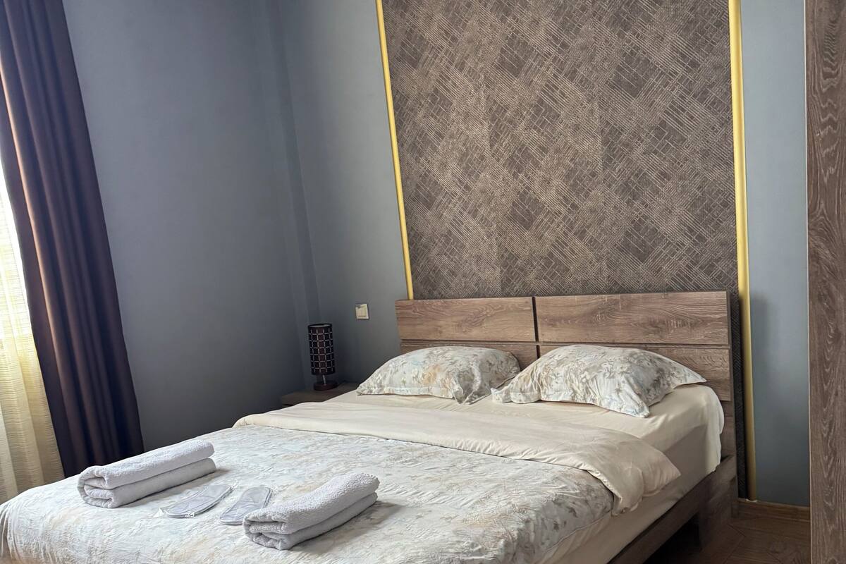 Ein ordentlich bezogenes Bett mit Handtüchern, einem Holzkopfschild und einer Wand mit Muster.