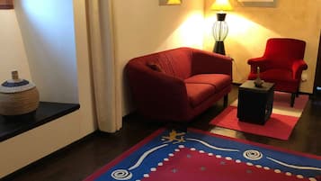 En stue med en rød sofa, en rød lænestol, et lille bord, en lampe og en dekorativ måtte.