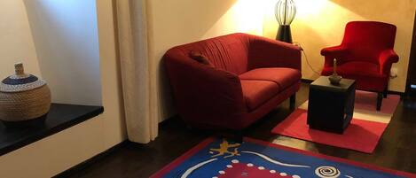 A living room with a red sofa, a red armchair, a small table, a lamp, and a decorative rug.