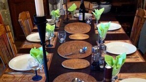 A long dining table set with plates, cutlery, and wine glasses, with woven placemats and green napkin holders. - Week end en Provence - Chambres d'hotes (Comps)