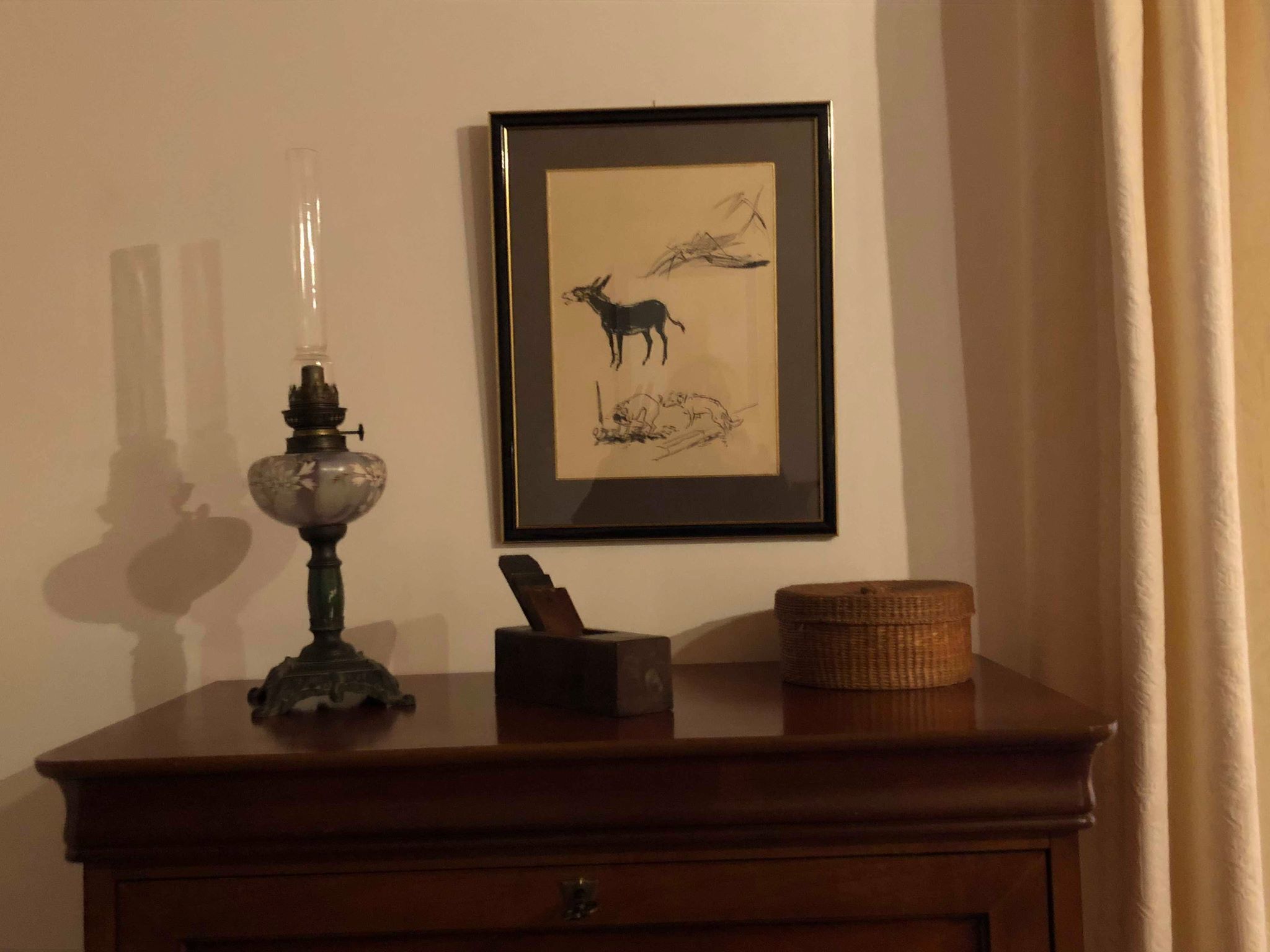 A wooden dresser with a lamp, a framed picture, and a basket.
