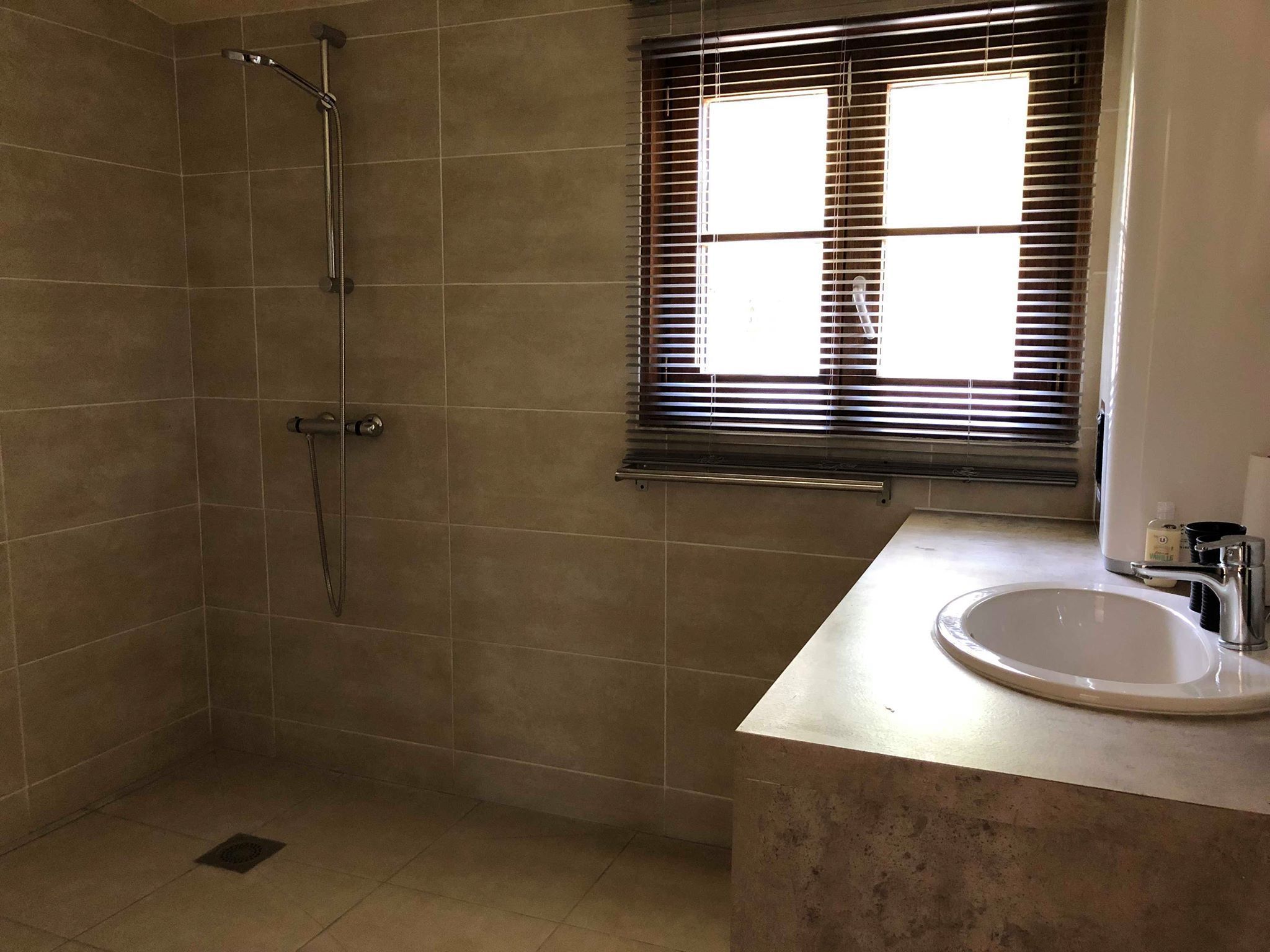 Un baño con ducha, lavamanos y ventana con persianas.