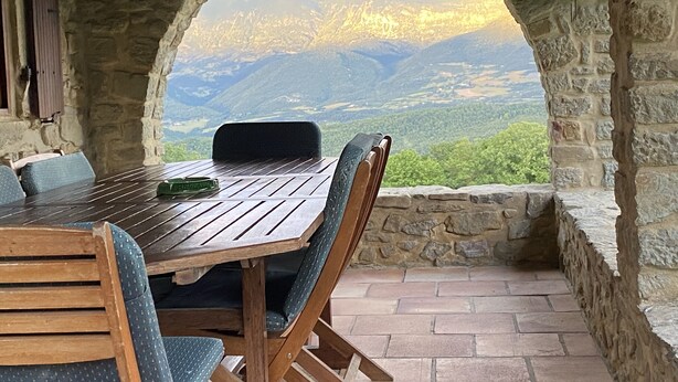 A stone-walled table and chairs with a view of mountains through an archway. - Week end en Provence - Chambres d'hotes (Comps)