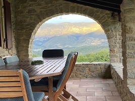 Mesa y sillas de piedra con vistas a montañas a través de un arco.