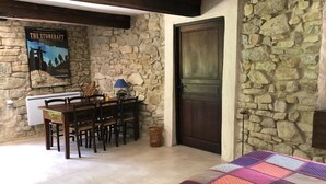 A cozy room with a stone wall, a wooden dining table with chairs, a quilt on the bed, and a poster on the wall. - Week end en Provence - Chambres d'hotes (Comps)