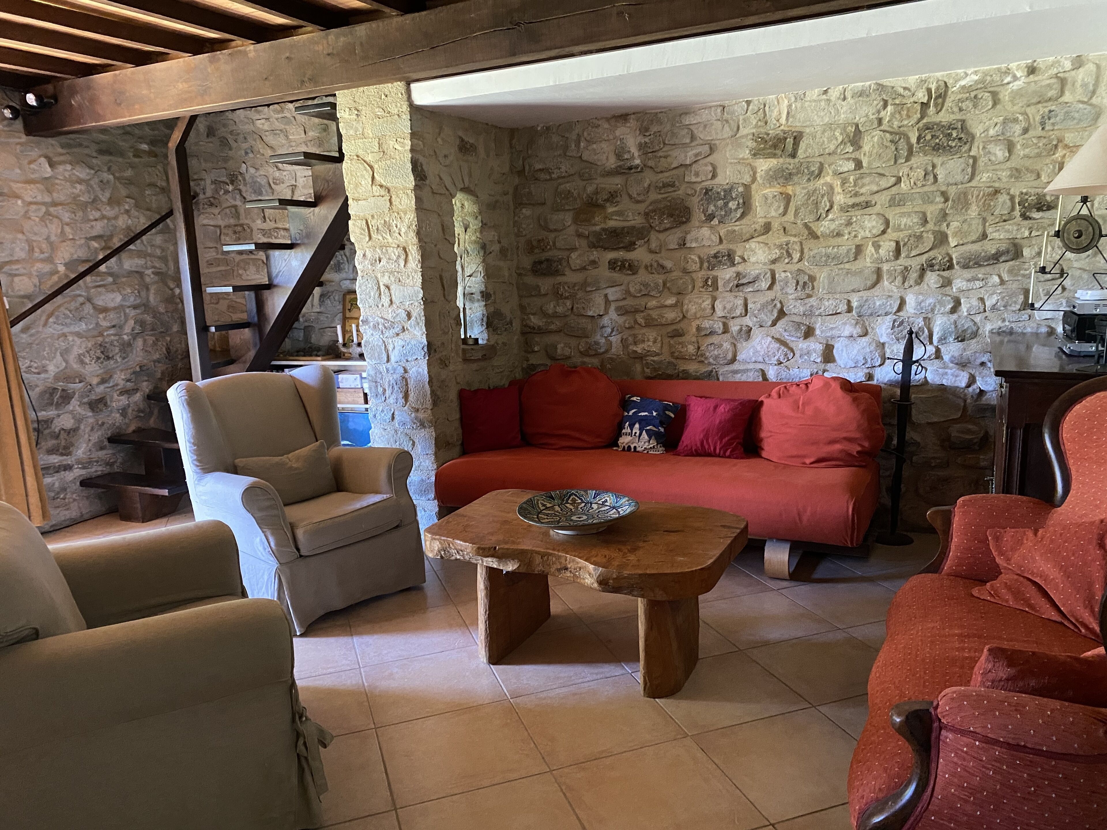 Un salon chaleureux avec un mur en pierre, un escalier en bois et un canapé rouge.