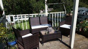 An outdoor patio with wicker furniture and a glass table, surrounded by a white fence and greenery. - Blue Peter Hotel (Stranraer)
