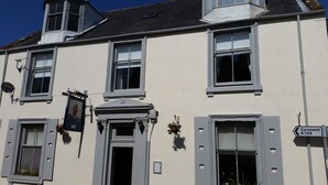 A building with multiple windows, a sign indicating 'Corsewall B738', and a hanging flower basket. - Blue Peter Hotel (Stranraer)