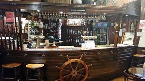 A bar with a wooden wheel, multiple taps, and a variety of bottles and glasses. - Blue Peter Hotel (Stranraer)