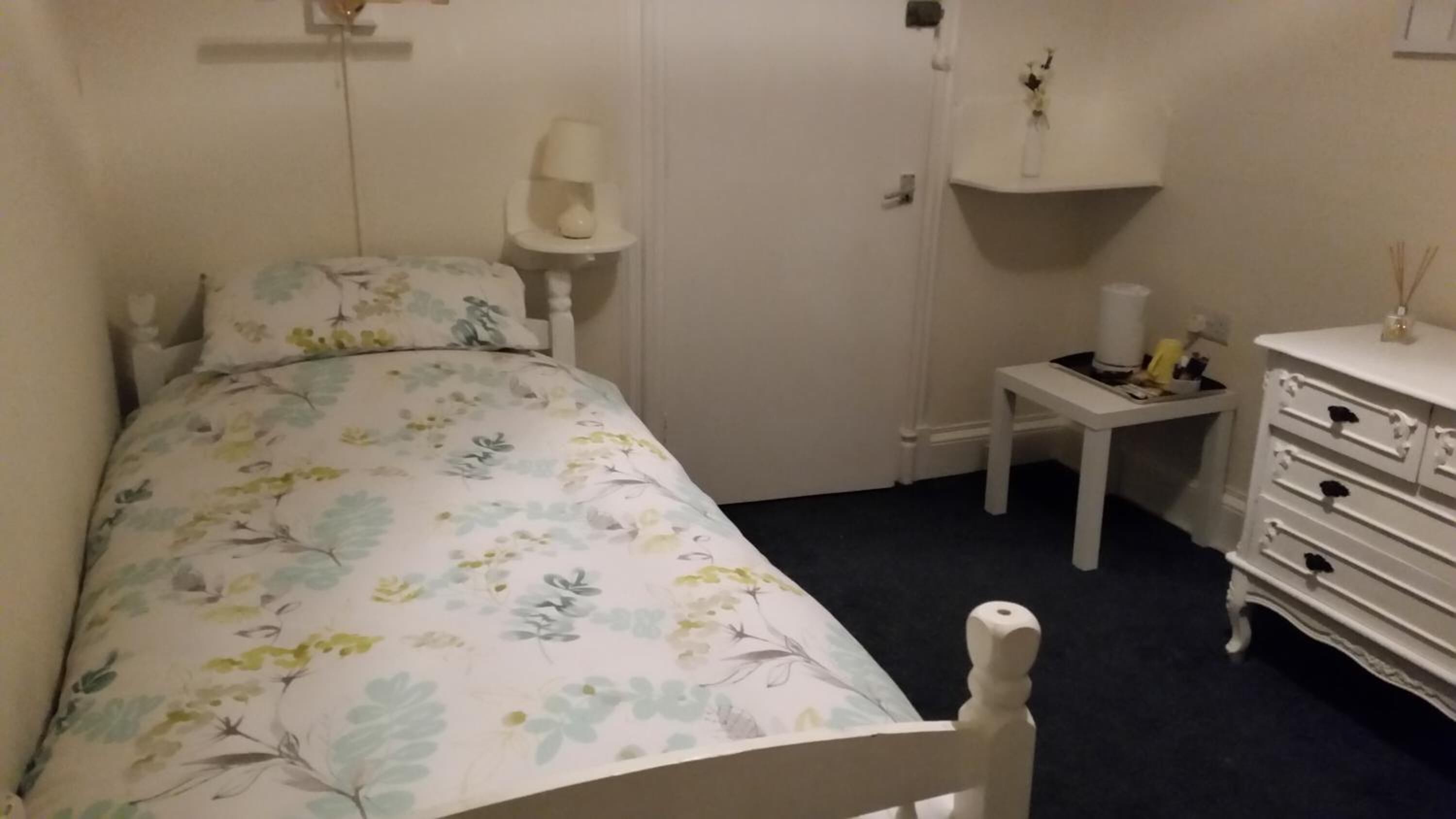A bedroom with a bed, a bedside table, a dresser, and a wall-mounted shelf.