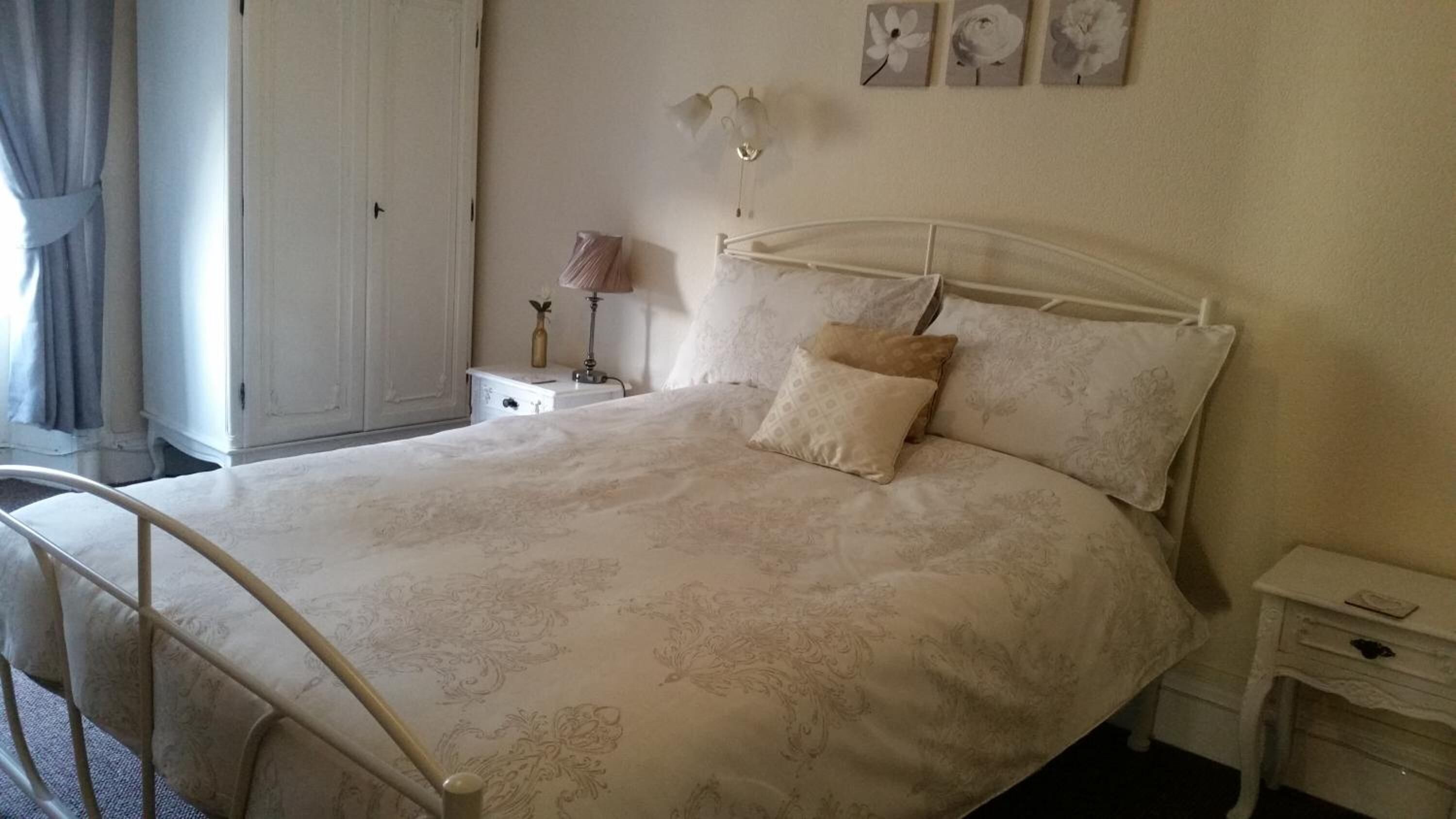 A neatly made bed with a floral-patterned bedspread, a bedside lamp, and a nightstand with a lamp.