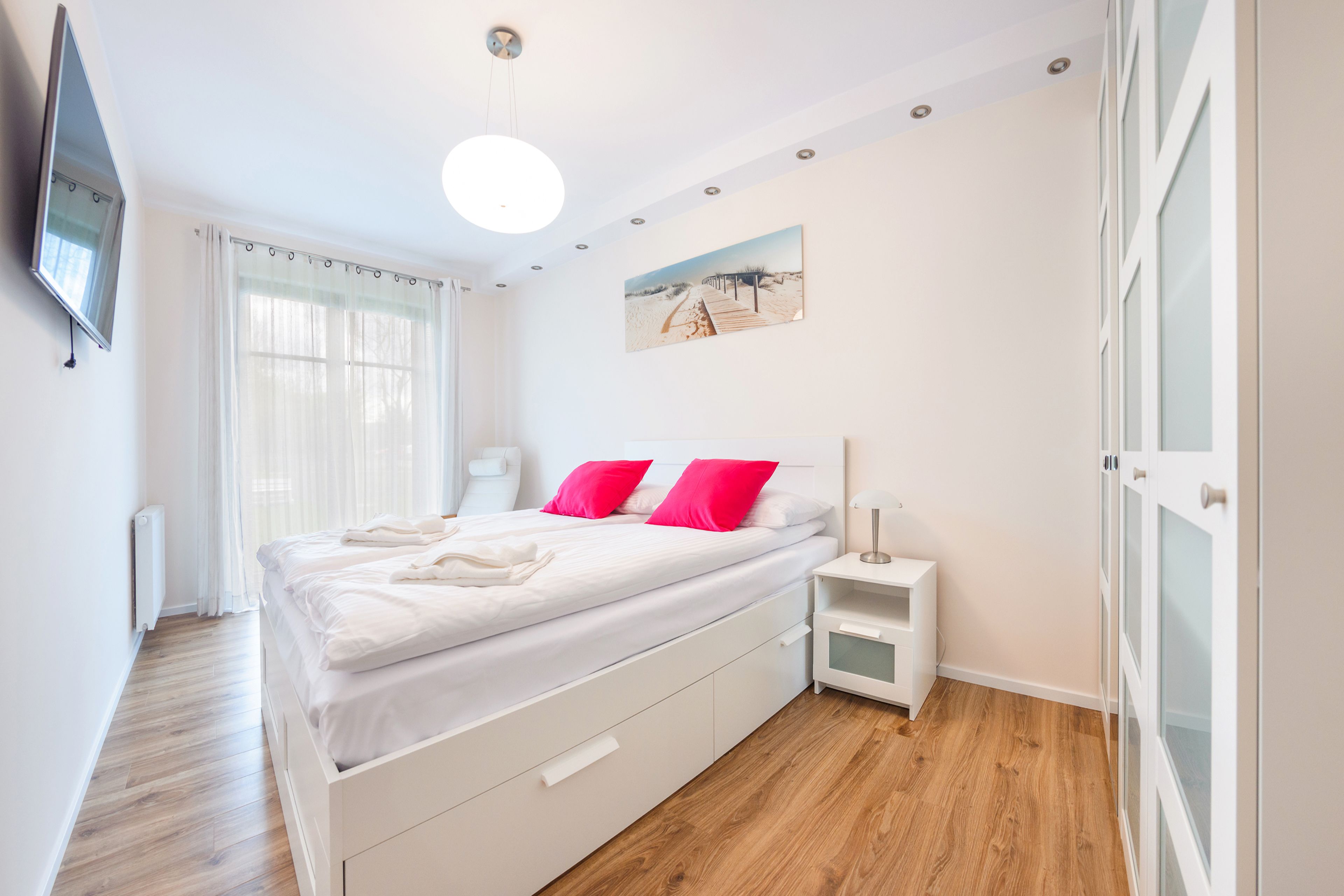 Una camera da letto moderna con un letto grande, comodini bianchi, una TV a parete e un quadro appeso al muro.