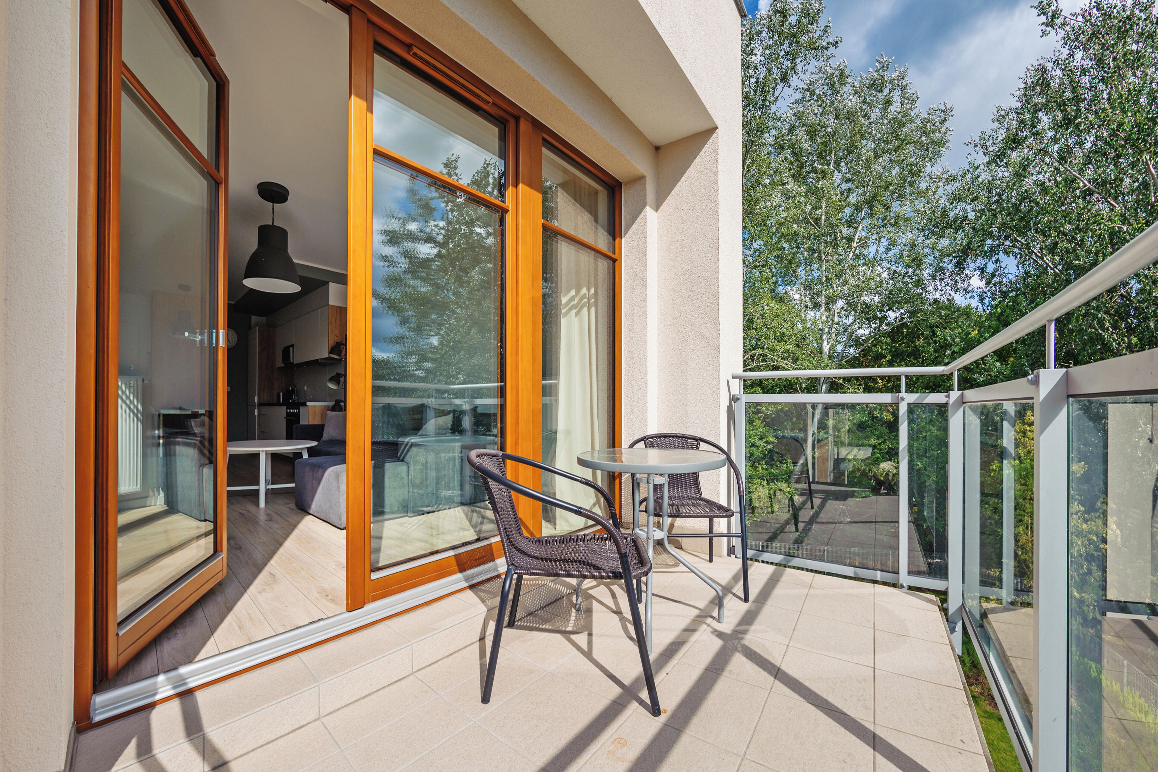 A balcony with a glass door leading to a dining area, wicker chairs, and a small table.