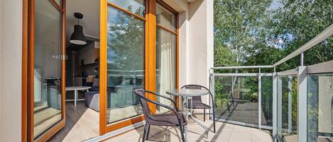 A balcony with a glass door leading to a dining area, wicker chairs, and a small table.