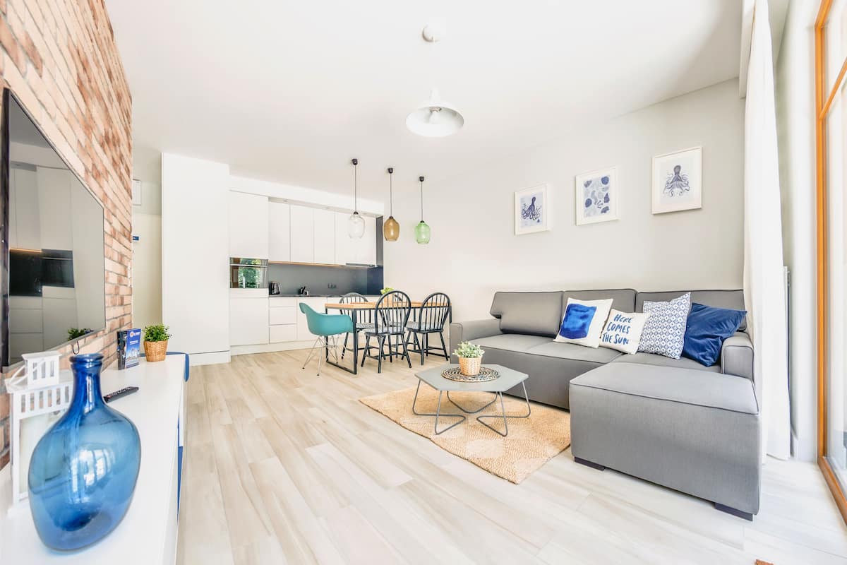 A modern living room with a grey sofa, a coffee table, and a dining area with chairs and a table.