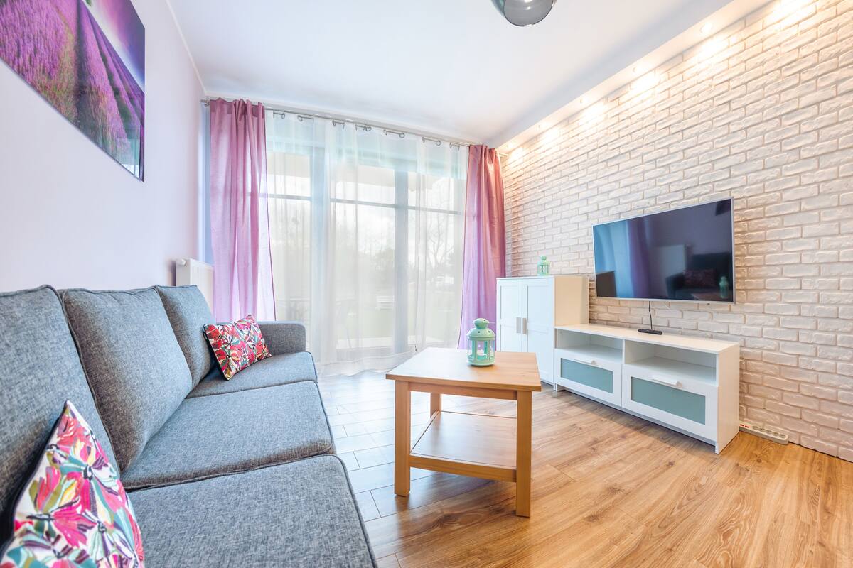 A modern living room with a grey sofa, a wooden coffee table, and a TV mounted on a brick wall.