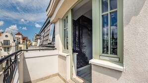 A residential building with a balcony, a window with a view of trees, and a door leading to an interior space.
