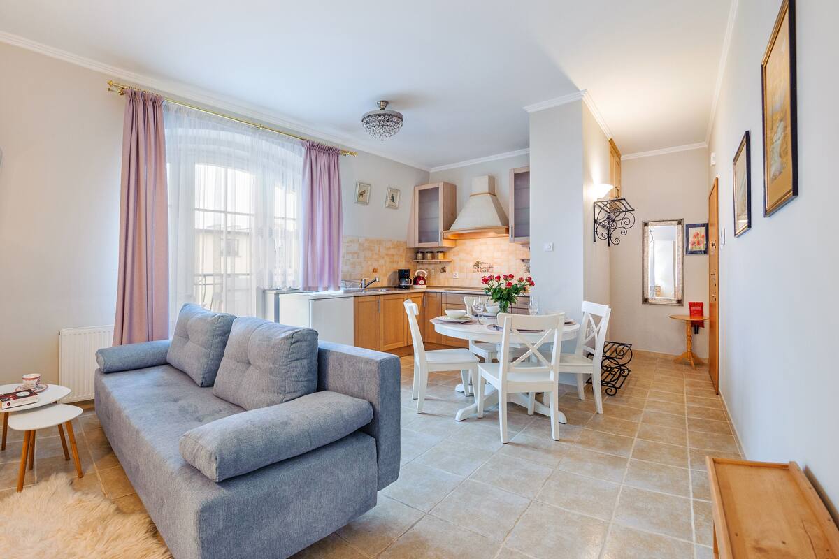 Un espace de vie compact comprenant un canapé gris, une petite table ronde et un coin repas avec des chaises blanches.