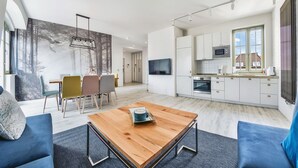A modern living room with a wooden coffee table, blue sofas, and a dining area with chairs.
