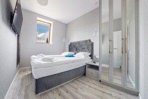 A modern bedroom with a bed, bedside table, and a large mirror. - Apartamenty Sun&Snow Przy Monte Cassino (Sopot)