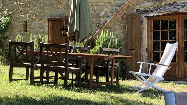 Un espacio de estar rústico al aire libre con pared de piedra, muebles de madera y una silla plegable blanca.
