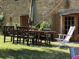 Un espacio de estar rústico al aire libre con pared de piedra, muebles de madera y una silla plegable blanca.