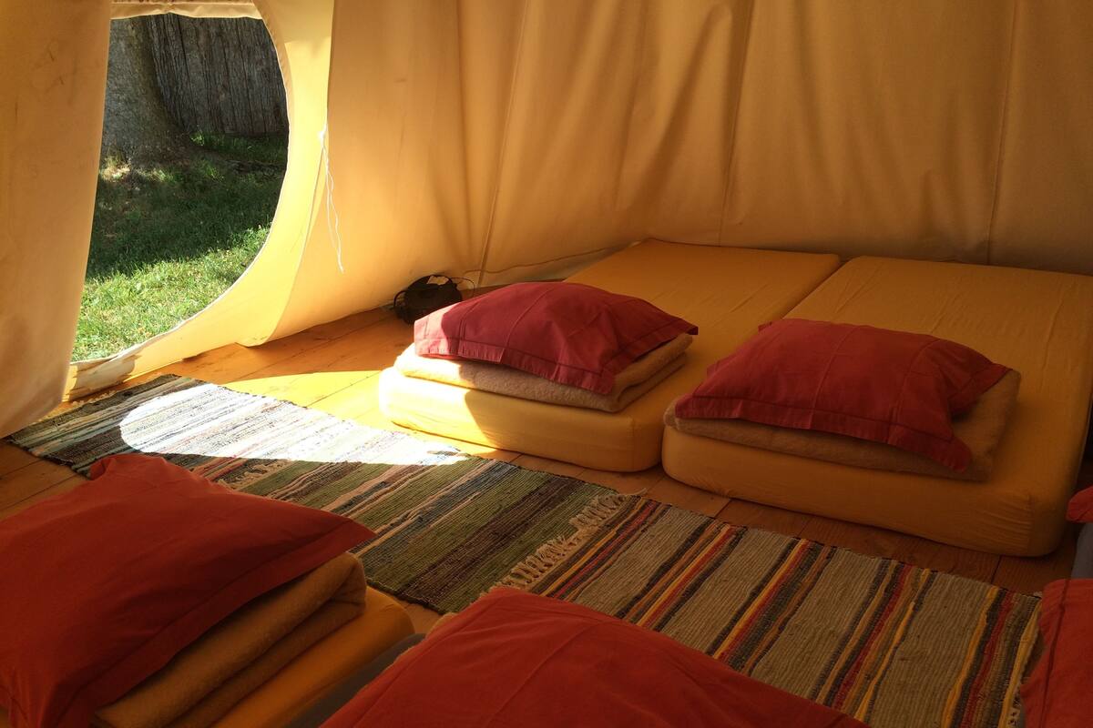 Une tente avec deux lits, chacun agrémenté d’oreillers rouges, et un tapis rayé sur le sol.