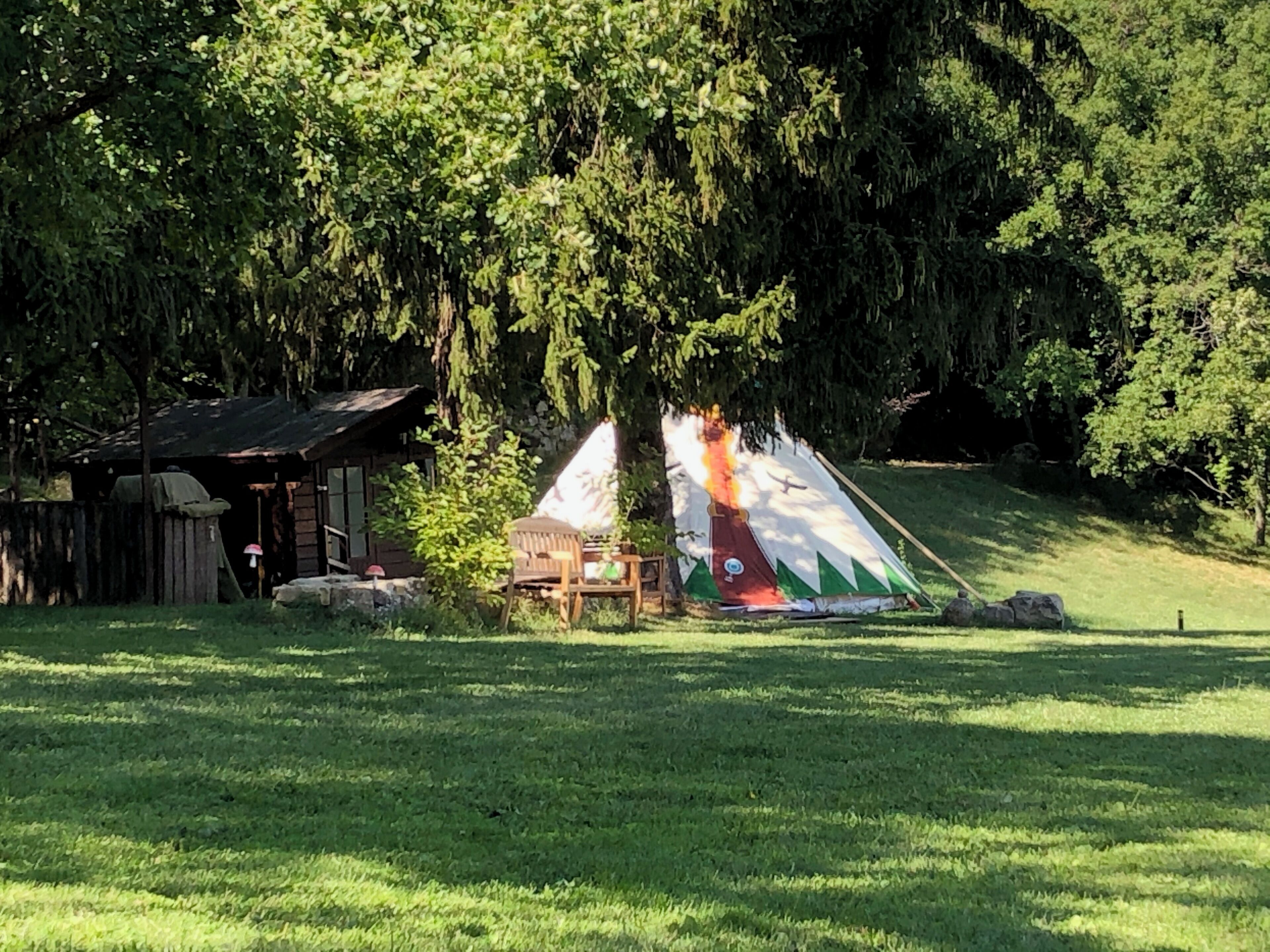 A rustic cabin with a small porch, a tent with a fire inside, and a grassy field.