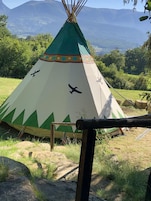 Un tipi con diseño verde y blanco, situado en un área con césped, rocas y árboles.