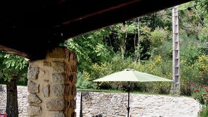 Un patio cubierto con paredes de piedra, mobiliario de exterior y una mesa con sombrilla verde.