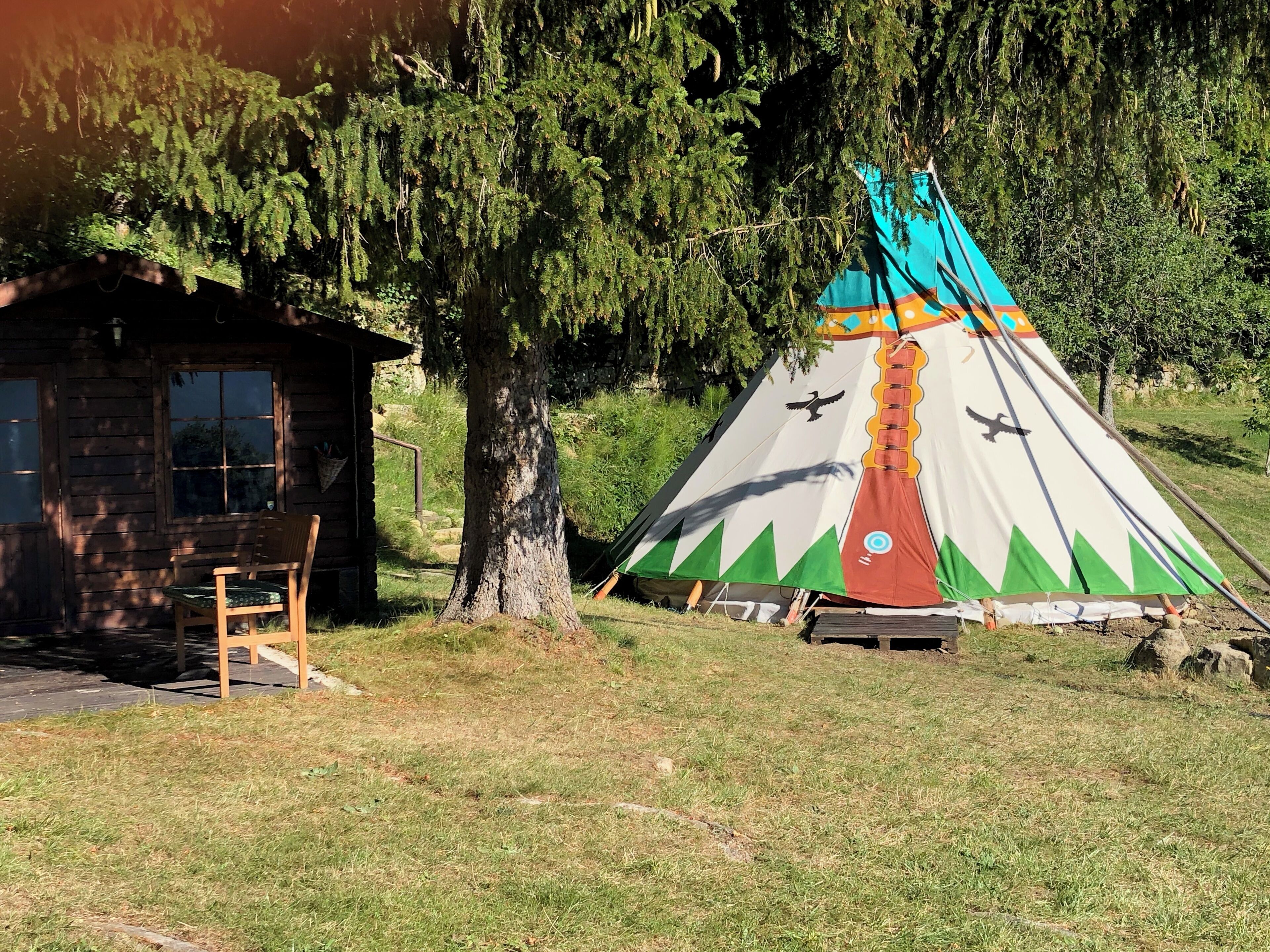 A wooden cabin with a single chair and a teepee with colorful patterns.