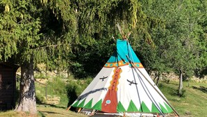 Un tipi tradicional con techo cónico, base de madera y un colorido diseño con aves y patrones geométricos.