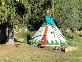 Un tipi tradicional con techo cónico, base de madera y un colorido diseño con aves y patrones geométricos.