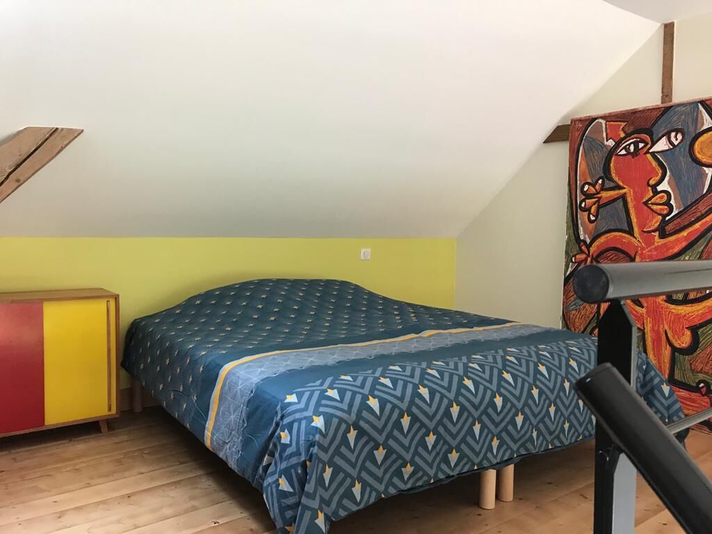 Una habitación pequeña con cama individual, techo inclinado, un cuadro colorido en la pared y suelo de madera.