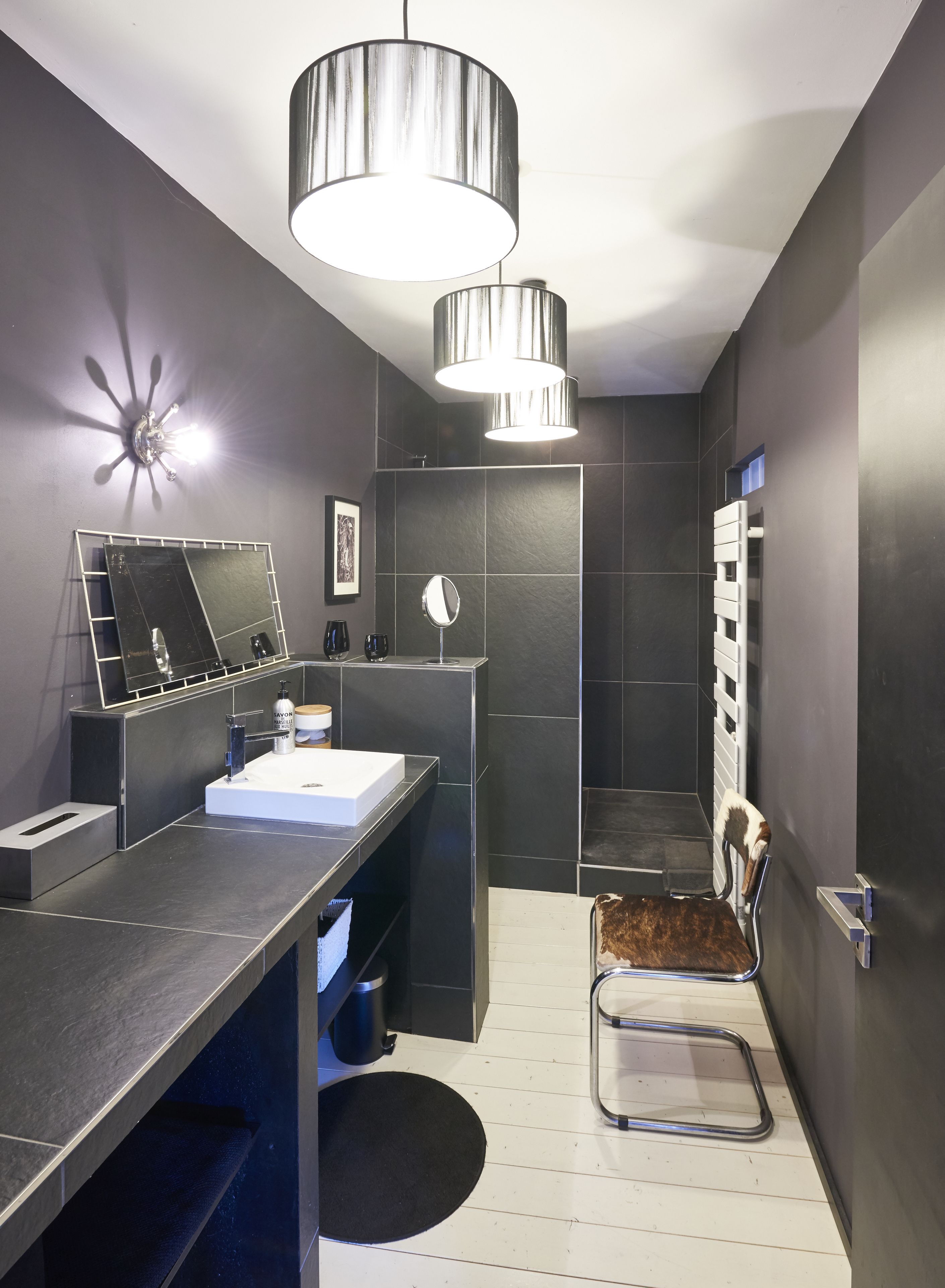 Un baño moderno con un espejo grande, un lavabo, una ducha y una silla.