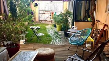 Een terras met een houten dek, tuinmeubilair en een kleine tuin met een pad.