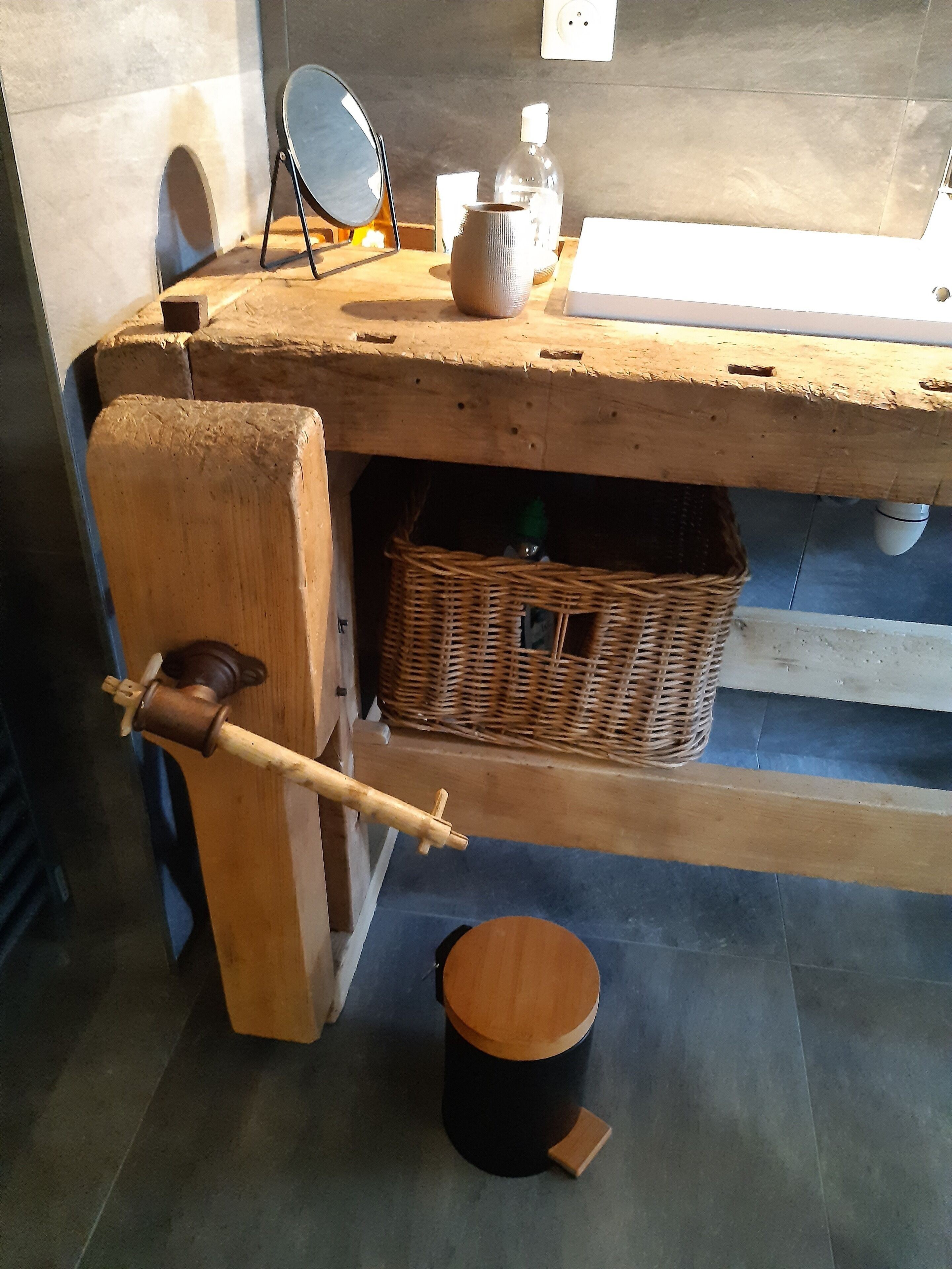 Une salle de bain rustique avec un lavabo en bois, un miroir, un distributeur de savon et un panier en osier.