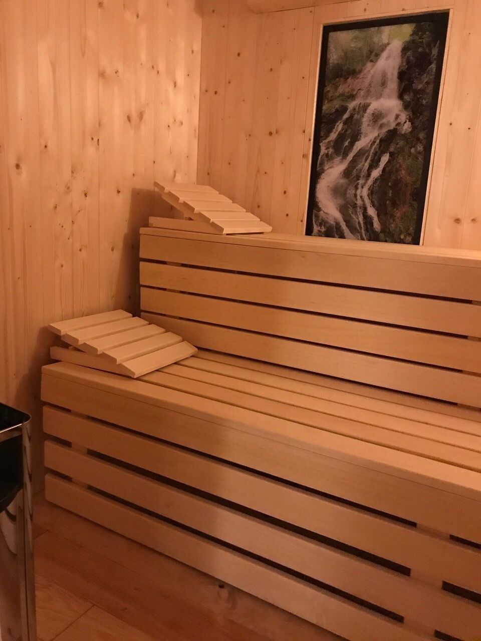 A wooden sauna bench with a waterfall painting on the wall.